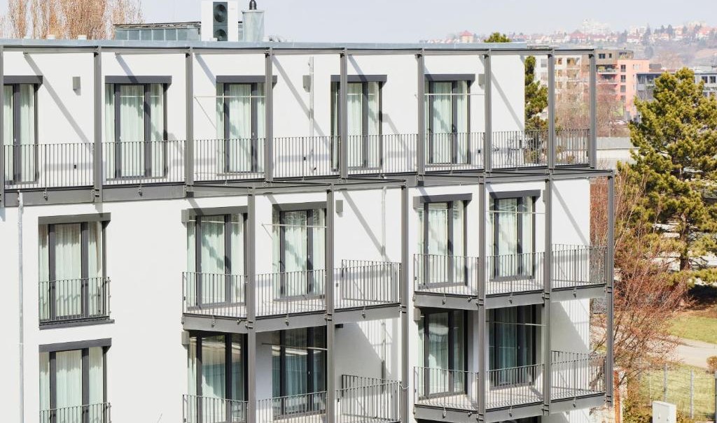 Modernes Wohngebäude mit mehreren Balkonen und großen Fenstern, umgeben von Bäumen und weiteren Gebäuden im Hintergrund., © livisit bergapartments Modernes Wohngebäude mit mehreren Balkonen und großen Fenstern, umgeben von Bäumen und weiteren Gebäuden im Hintergrund., © livisit bergapartments