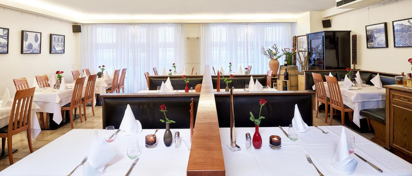 Elegant restaurant with white tablecloths, wooden chairs and decorative roses on the tables. Bright, inviting atmosphere., © Frank Pham