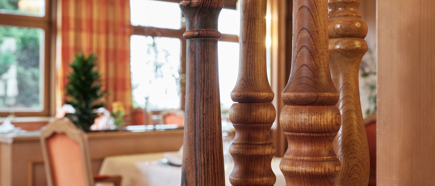 Große Holz-Pfeffermühlen stehen auf einem Marmortisch in einem eleganten Restaurant mit Holzeinrichtung und orangefarbenen Stühlen., © Badhotel Restaurant Stauferland