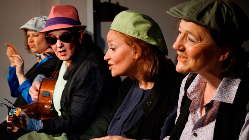 Vier Personen auf einer B&uuml;hne, eine spielt Gitarre. Sie tragen bunte H&uuml;te und sind in eine lebhafte Unterhaltung vertieft., &copy; Katja Ritter