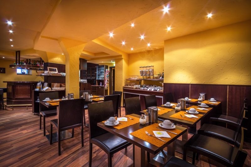 A cozy breakfast room with laid tables, warm lighting and a buffet in the background., &copy; TOMAS