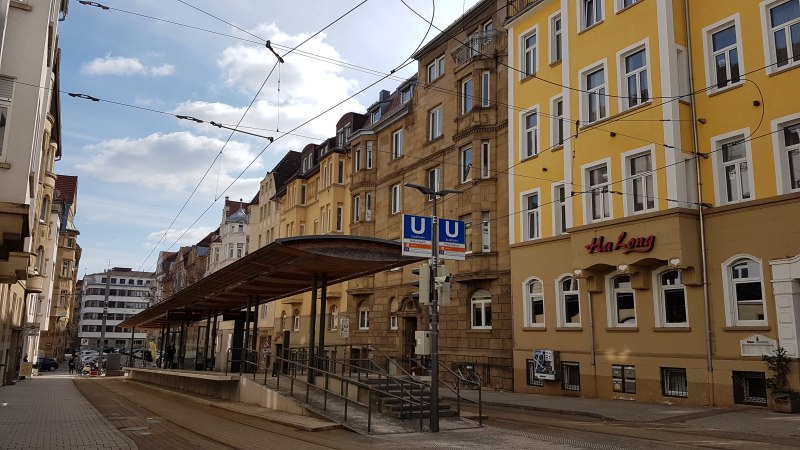 Straßenbahnhaltestelle in einer städtischen Straße, umgeben von alten Gebäuden. Ein Restaurant namens Ha Long ist zu sehen., © SMG Straßenbahnhaltestelle in einer städtischen Straße, umgeben von alten Gebäuden. Ein Restaurant namens Ha Long ist zu sehen., © SMG