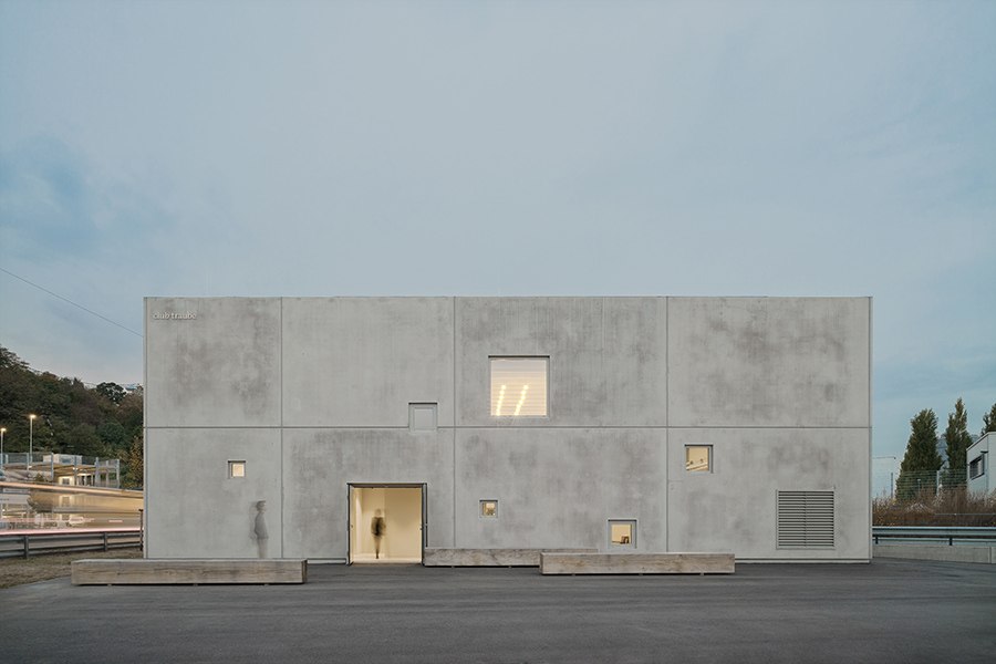 Ein modernes Gebäude mit Betonfassade und kleinen Fenstern. Die minimalistische Architektur hebt sich gegen den blauen Himmel ab., © club traube Ein modernes Gebäude mit Betonfassade und kleinen Fenstern. Die minimalistische Architektur hebt sich gegen den blauen Himmel ab., © club traube