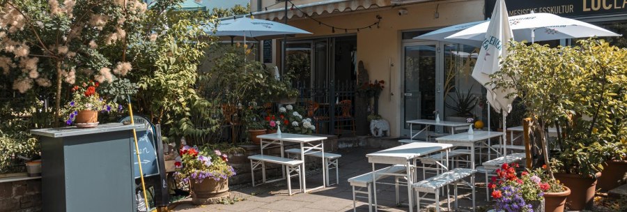 Cosy outdoor area of a café with white tables and chairs, surrounded by lush plants and colorful flowers., © SMG Stuttgart Marketing GmbH - Sarah Schmid