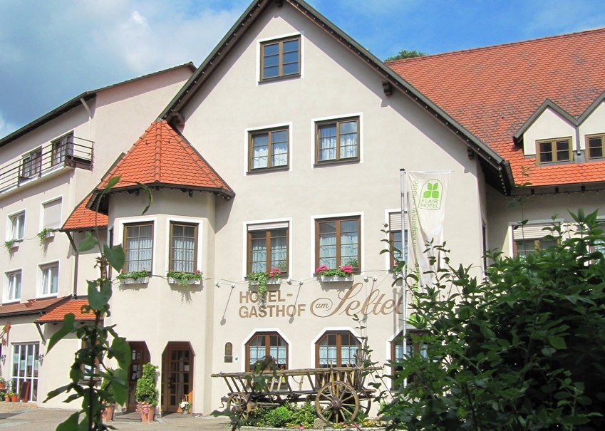Hotel-Gasthof mit traditionellem Fachwerk, Blumenkästen und einem alten Holzwagen davor. Der Himmel ist blau mit einigen Wolken., © R.Storr Hotel-Gasthof mit traditionellem Fachwerk, Blumenkästen und einem alten Holzwagen davor. Der Himmel ist blau mit einigen Wolken., © R.Storr