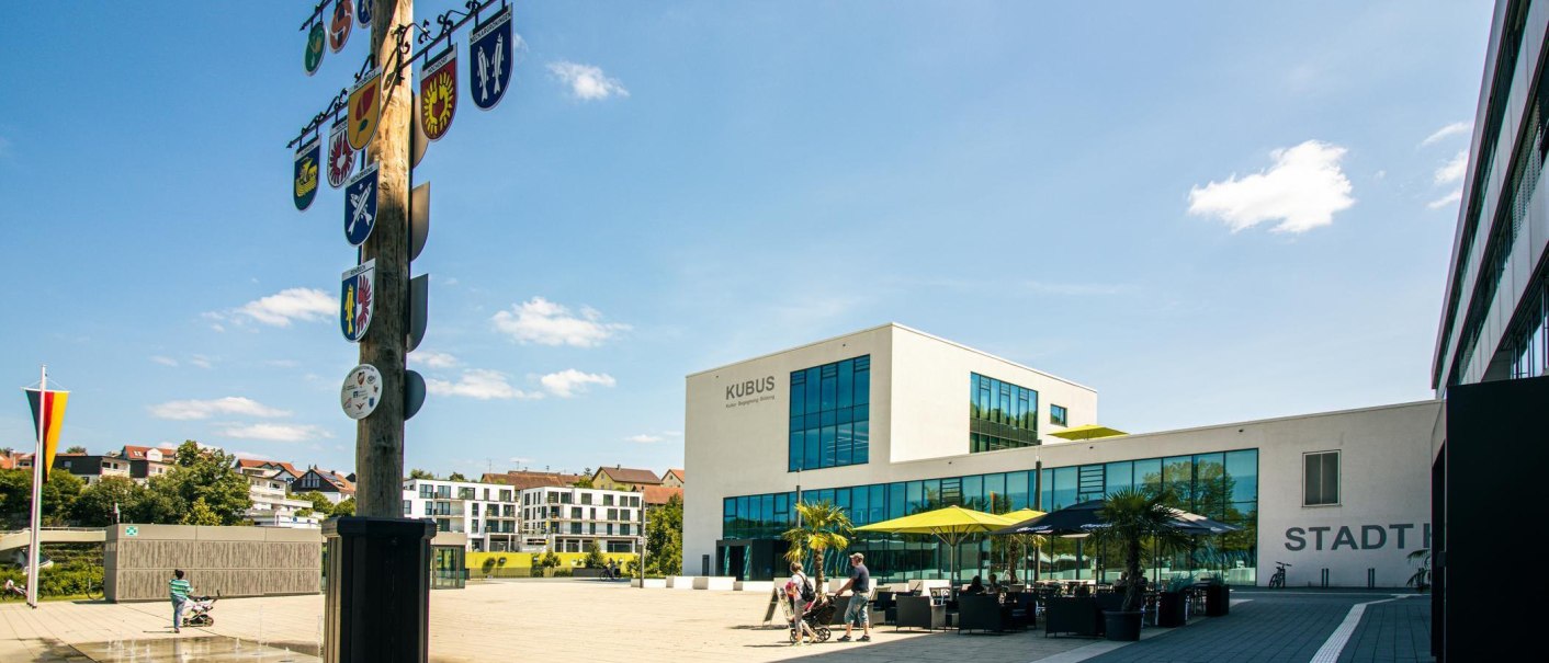 Modern market square in Remseck with the 'KUBUS' building, a maypole with a coat of arms and people out for a walk. Sunny day with blue sky., © Stuttgart-Marketing GmbH, Sarah Schmid