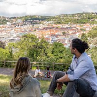 Zwei Personen sitzen auf einer Wiese und schauen auf die Stadt Stuttgart. Im Hintergrund sind Hügel und Gebäude zu sehen, darunter der Fernsehturm., © SMG, Martina Denker Zwei Personen sitzen auf einer Wiese und schauen auf die Stadt Stuttgart. Im Hintergrund sind Hügel und Gebäude zu sehen, darunter der Fernsehturm., © SMG, Martina Denker