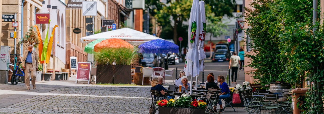 Gem&uuml;tliche Stra&szlig;enszene im Bohnenviertel mit Caf&eacute;s, bunten Sonnenschirmen und Menschen, die im Freien sitzen. Pflastersteine und gr&uuml;ne Pflanzen s&auml;umen den Weg., &copy; SMG Thomas Niederm&uuml;ller