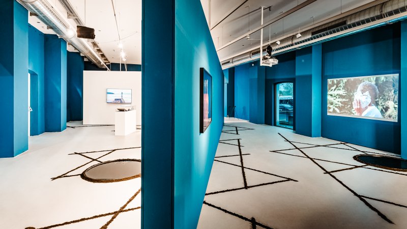 Modern gallery with blue walls, video installations and geometric patterns on the floor. Industrial design with visible ventilation pipes., © Publication only by client - disclosure to third parties only after consultation. Modern gallery with blue walls, video installations and geometric patterns on the floor. Industrial design with visible ventilation pipes., © Publication only by client - disclosure to third parties only after consultation.