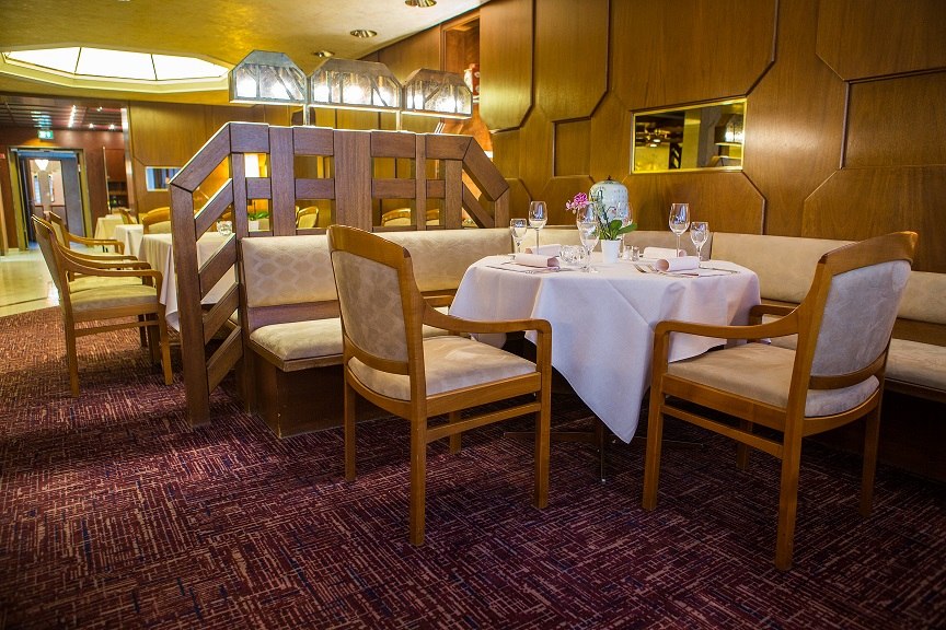 Elegantes Restaurant mit Holzmöbeln, gedecktem Tisch und gemütlicher Beleuchtung. Teppichboden und dekorative Trennwand im Hintergrund., © Hotel Royal