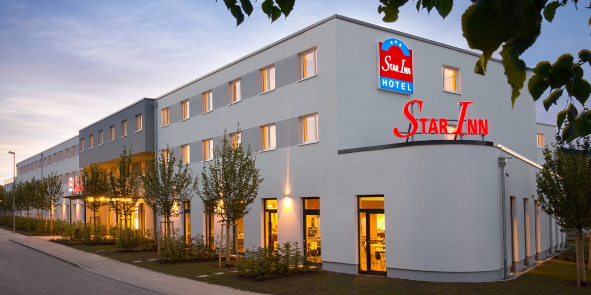 Moderne Hotelaußenansicht bei Dämmerung, beleuchtet mit dem Namen Star Inn. Mehrere Fenster und Bäume vor dem Gebäude., © Star Inn Stuttgart Airport-Messe Moderne Hotelaußenansicht bei Dämmerung, beleuchtet mit dem Namen Star Inn. Mehrere Fenster und Bäume vor dem Gebäude., © Star Inn Stuttgart Airport-Messe