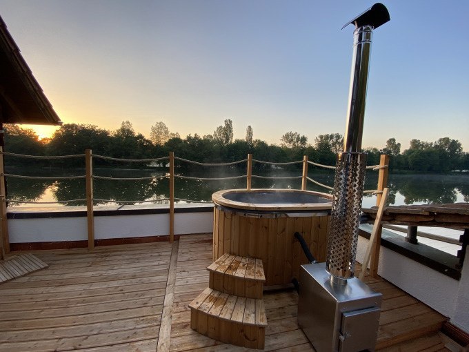 Wooden terrace with hot tub, next to a stove. In the background a river and trees at sunset., &copy; Cool-Tours StattReisen