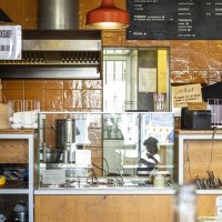 Ein Imbiss mit Getr&auml;nkek&uuml;hlschrank, Theke und Men&uuml;tafel. Eine Person arbeitet hinter der Theke. Die W&auml;nde sind orange gefliest., &copy; SMG, Sarah Schmid