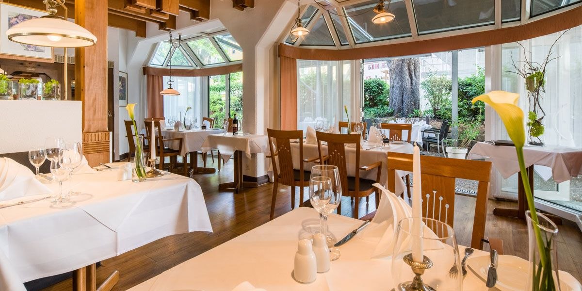 Elegantes Restaurant mit weißen Tischdecken, Holzstühlen und großen Fenstern, die einen Blick auf den Garten bieten., © Best Western Plus Hotel am Schlossberg
