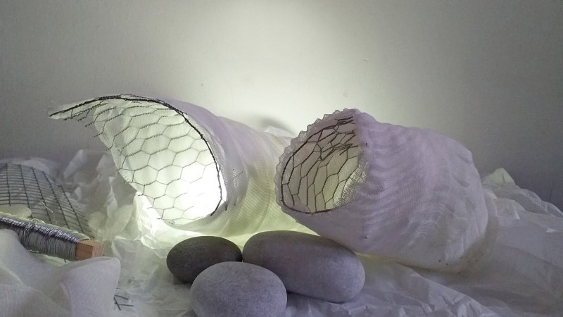 Zwei modellierte Kokons aus Drahtgeflecht und Stoff, beleuchtet und von Steinen umgeben, auf einem weißen Hintergrund., © StadtPalais Zwei modellierte Kokons aus Drahtgeflecht und Stoff, beleuchtet und von Steinen umgeben, auf einem weißen Hintergrund., © StadtPalais