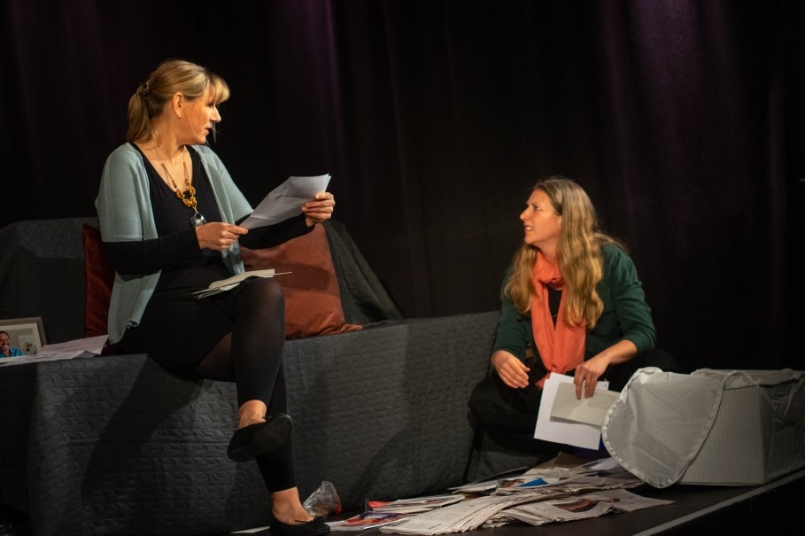 Zwei Frauen auf einer Bühne, eine sitzt auf einem Sofa, die andere auf dem Boden. Sie halten Papiere in der Hand, umgeben von verstreuten Dokumenten., © Improtheater Stuttgart Zwei Frauen auf einer Bühne, eine sitzt auf einem Sofa, die andere auf dem Boden. Sie halten Papiere in der Hand, umgeben von verstreuten Dokumenten., © Improtheater Stuttgart