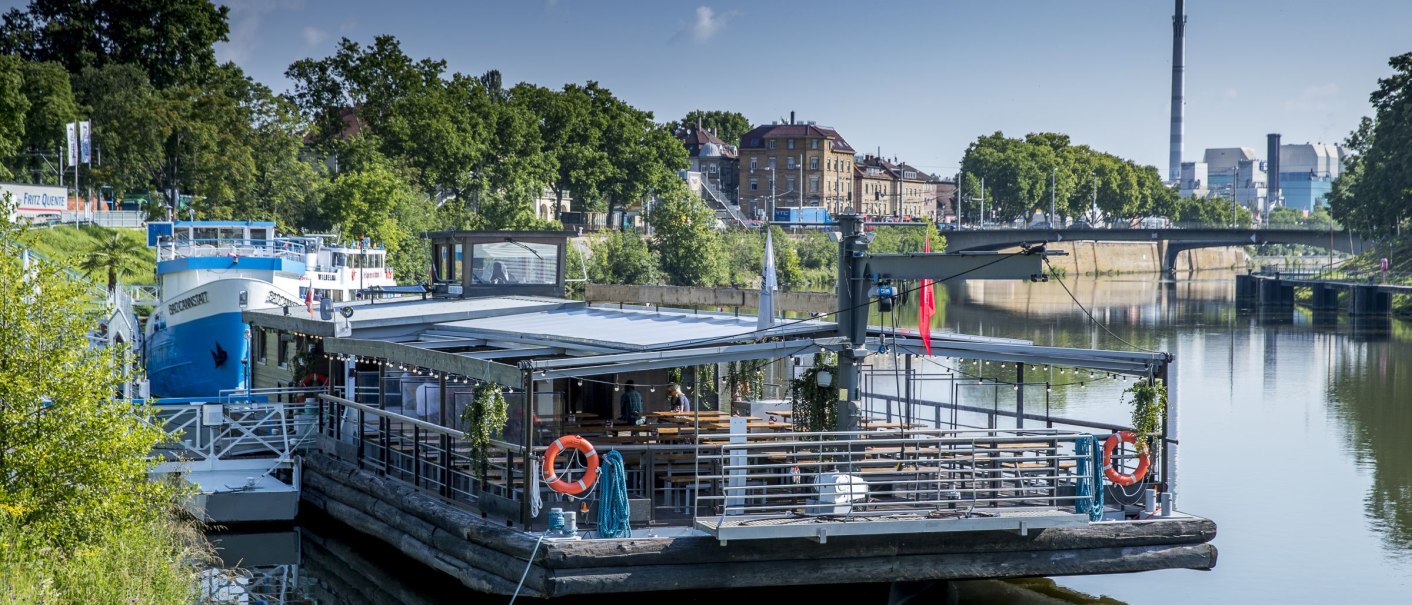 A floating restaurant on the Neckar, surrounded by green vegetation and urban buildings in the background., © all copyrights are reserved by maks richter