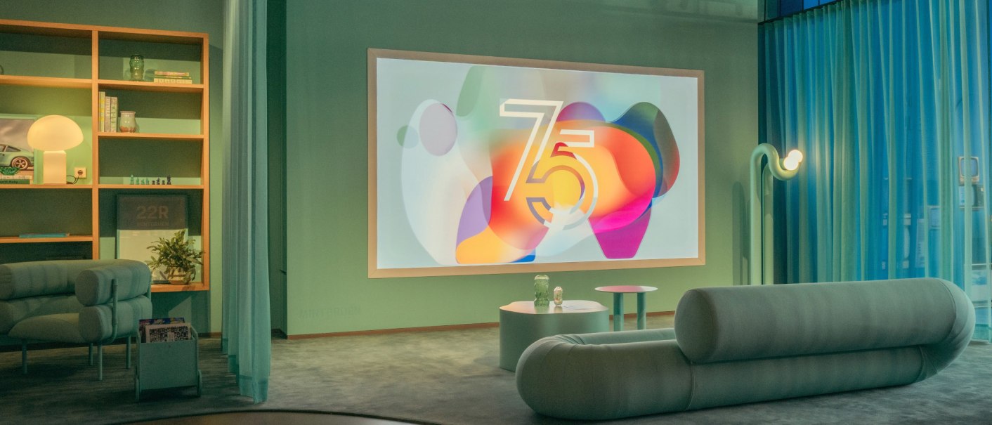 Modern room with sofa, shelf and large screen showing the number 75. Stylish lighting and decoration., © Porsche AG