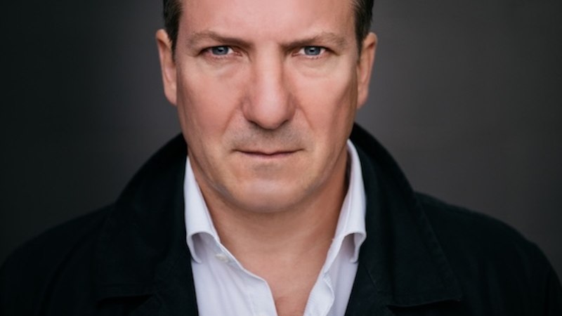 Ein Mann in einem dunklen Mantel und weißem Hemd blickt ernst in die Kamera, vor einem dunklen Hintergrund., © Renitenztheater Stuttgart e.V. Ein Mann in einem dunklen Mantel und weißem Hemd blickt ernst in die Kamera, vor einem dunklen Hintergrund., © Renitenztheater Stuttgart e.V.