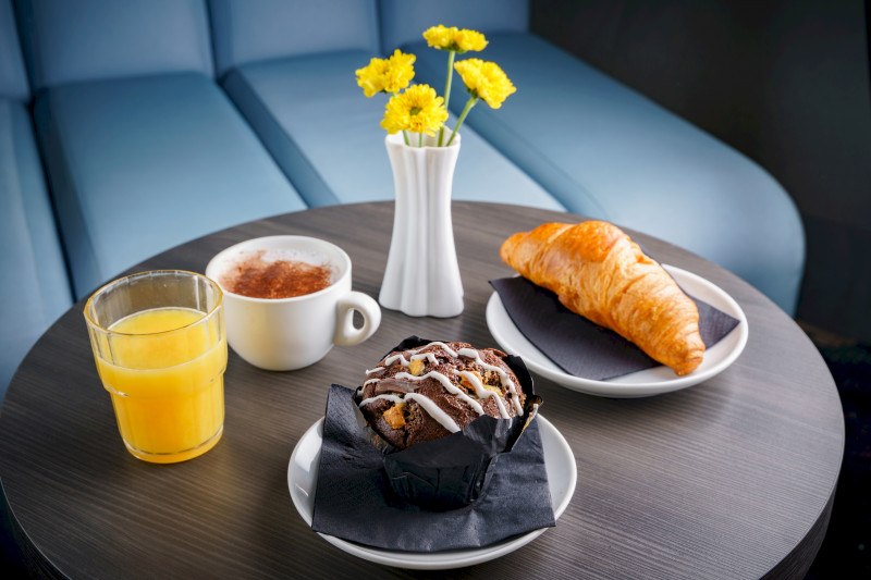 A table with croissant, chocolate muffin, orange juice, cappuccino and yellow flowers in a vase., © A&O Hostels Marketing GmbH A table with croissant, chocolate muffin, orange juice, cappuccino and yellow flowers in a vase., © A&O Hostels Marketing GmbH