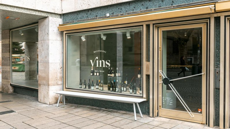 Schaufenster des Weinhandels 'Vins Gute Weine' mit Weinflaschen im Display und einer Bank davor., &copy; SMG, Sarah Schmid
