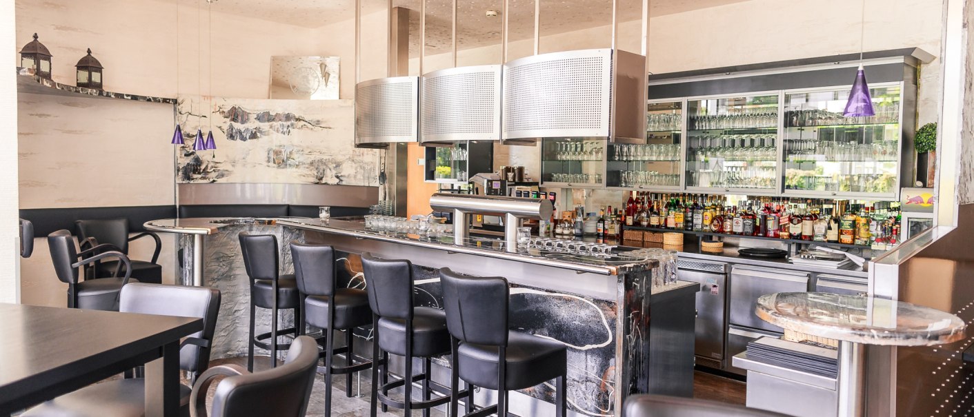 Modern bar with black stools, well-stocked counter and glasses in the background. Stylish lighting and decoration., © PLAZA Hotelgroup GmbH