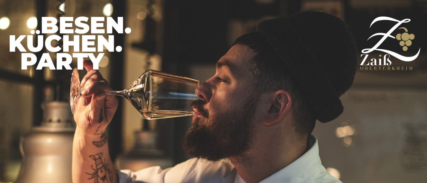 Ein Mann mit Bart genie&szlig;t ein Glas Wein. Im Hintergrund das Logo des Weinguts Zai&szlig;. Text: Besen-K&uuml;chen-Party., &copy; Weingut Zai&szlig;