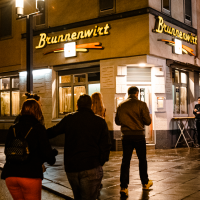 Nachtaufnahme eines Restaurants namens Brunnenwirt. Mehrere Personen stehen davor, die Straße ist nass und ein E-Scooter ist am Rand geparkt., © Stuttgart-Marketing GmbH, Sarah Schmid Nachtaufnahme eines Restaurants namens Brunnenwirt. Mehrere Personen stehen davor, die Straße ist nass und ein E-Scooter ist am Rand geparkt., © Stuttgart-Marketing GmbH, Sarah Schmid