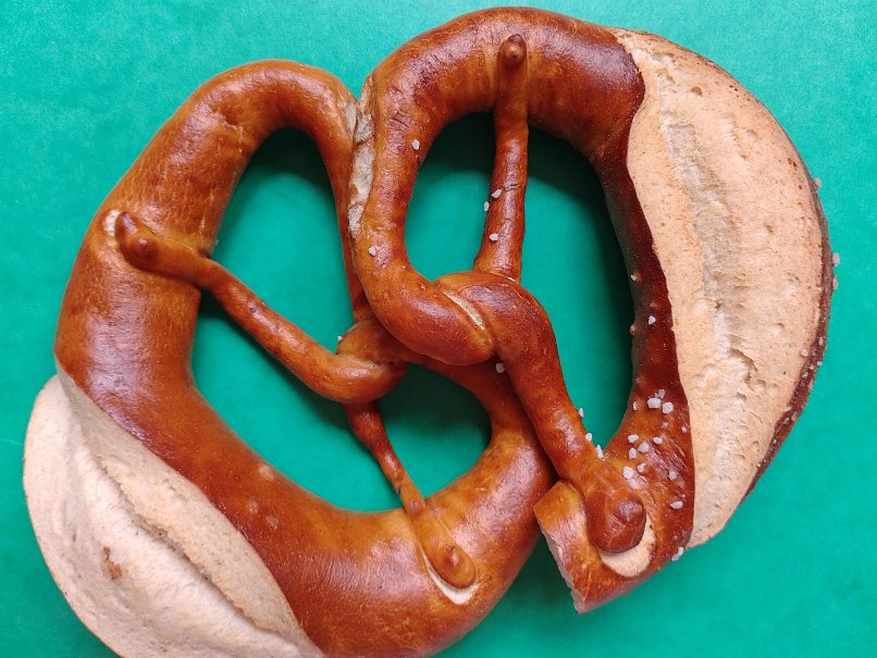 Eine Brezel liegt auf einem grünen Hintergrund. Die Brezel ist goldbraun mit grobem Salz bestreut., © Svenja Rehse