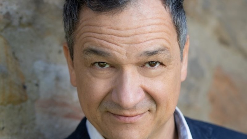 Ein Mann in einem dunklen Anzug und weißem Hemd steht vor einer Steinwand und schaut direkt in die Kamera., © Renitenztheater Stuttgart e.V. Ein Mann in einem dunklen Anzug und weißem Hemd steht vor einer Steinwand und schaut direkt in die Kamera., © Renitenztheater Stuttgart e.V.