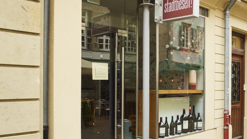Eingang eines Gesch&auml;fts mit dem Schild 'Stadtbesen'. In der Vitrine stehen Weinflaschen. Eine rote Leuchtreklame ist an der Wand angebracht., &copy; Stuttgart-Marketing GmbH, Sarah Schmid