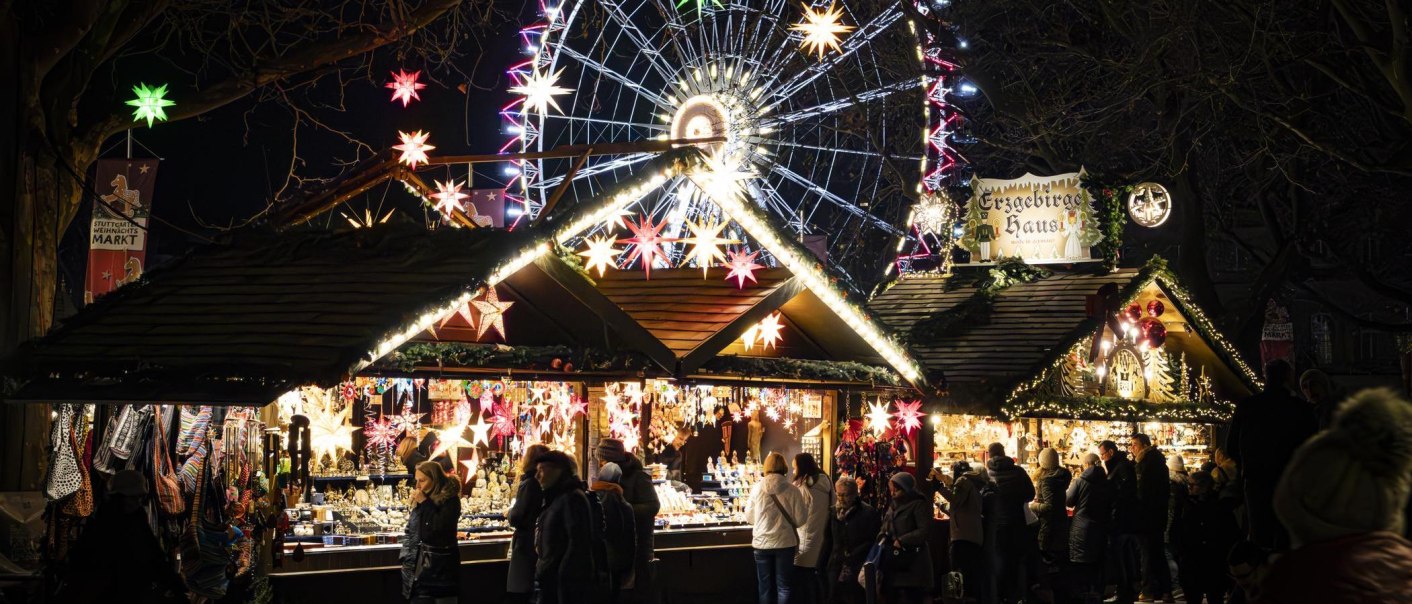 Stuttgarter Weihnachtsmarkt bei Nacht mit beleuchteten Ständen, bunten Sternen und einem großen Riesenrad im Hintergrund., © Stuttgart-Marketing GmbH, Sarah Schmid