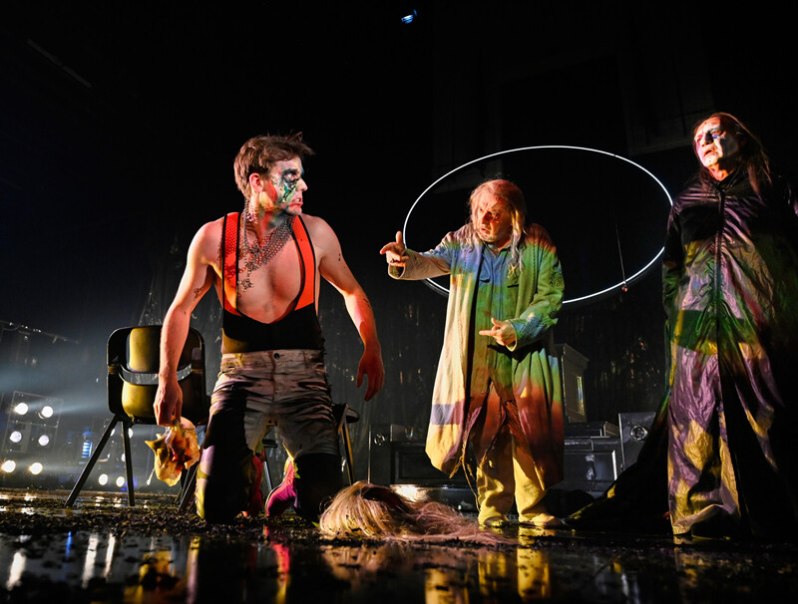 Three actors in colorful costumes on a stage. One kneels while the others stand. The scene is dramatically lit., &copy; W&uuml;rttembergische Staatstheater Stuttgart