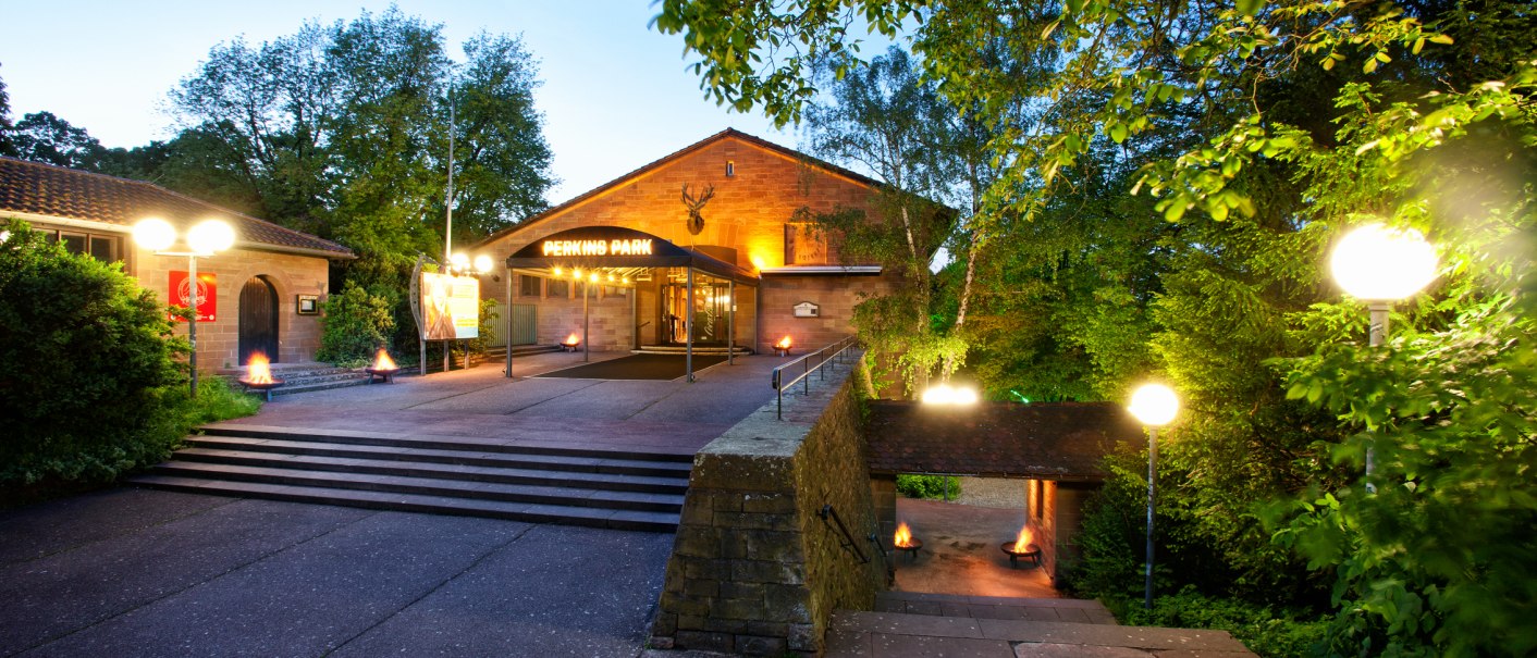 Eingang des Perkins Park in Stuttgart bei D&auml;mmerung, umgeben von B&auml;umen und beleuchtet mit Laternen., &copy; PerkinsPark