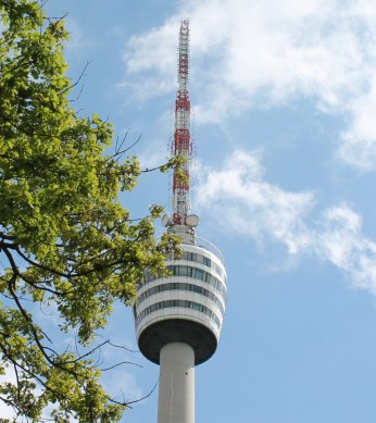 The Stuttgart television tower rises into the blue sky, surrounded by green tree branches., © Stuttgart-Marketing GmbH