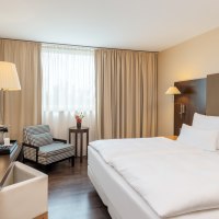 Modern double room with large bed, desk, armchair and window with beige curtains. A TV and a floor lamp are also available., &copy; NH Hotel Stuttgart Airport