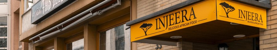 Restaurant Injeera with yellow sign and wooden fence, offers African cuisine. Exterior view with lanterns and plants., © SMG Stuttgart Marketing GmbH - Sarah Schmid