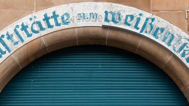 Ein altes Schild &uuml;ber einem Torbogen tr&auml;gt die Aufschrift 'Gastst&auml;tte zum Wei&szlig;en Ro&szlig;'. Der Hintergrund ist ein geschlossenes, blaues Rolltor., &copy; Stuttgart-Marketing GmbH, Sarah Schmid