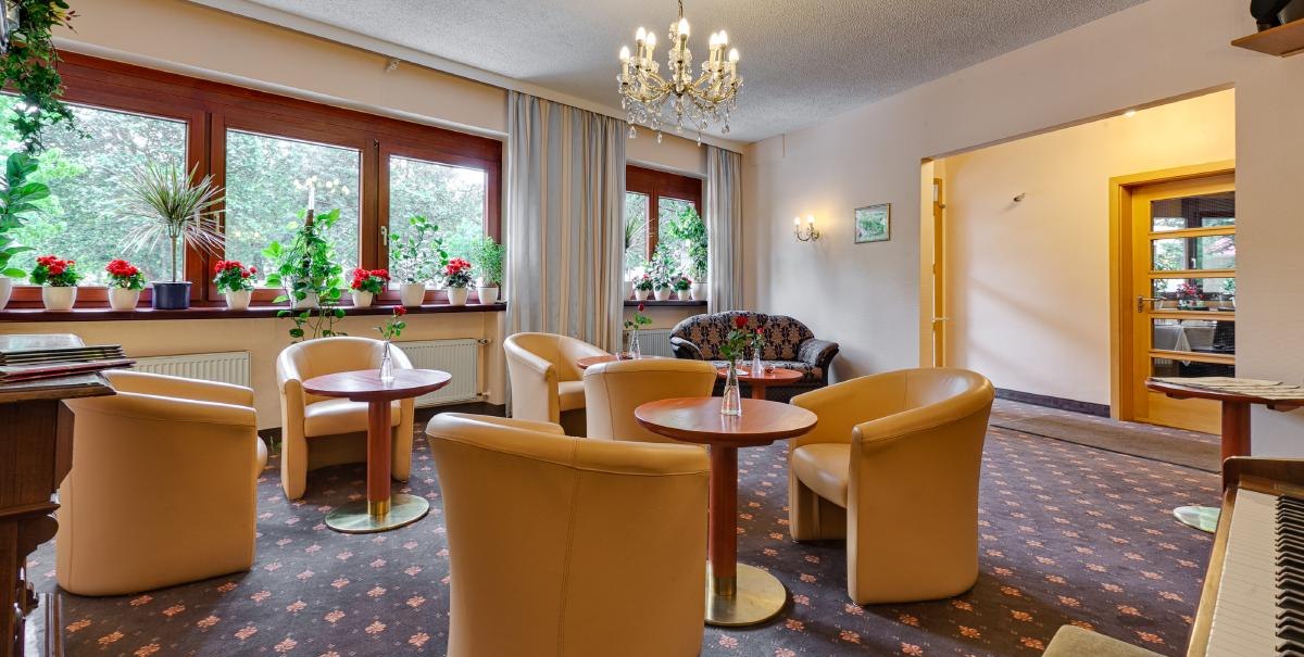 Gem&uuml;tliche Hotel-Lobby mit beigen Sesseln, Holztischen und Pflanzen am Fenster. Ein Kronleuchter h&auml;ngt von der Decke., &copy; ARNOTEL GmbH