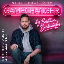 Ein Mann sitzt vor einem leuchtenden Schild mit der Aufschrift 'GameChanger by Bastian Bielendorfer'. Er trägt eine Jeansjacke und einen grauen Hoodie., © links im Bild