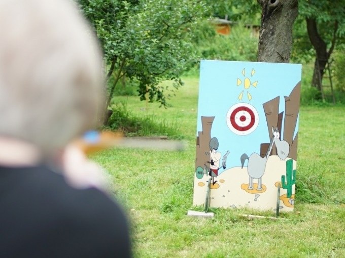 Person aims a blowpipe at a painted wooden board with a target outside., &copy; Cool-Tours StattReisen