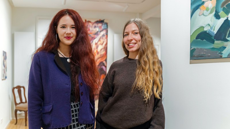 Zwei Frauen in einer Kunstgalerie, umgeben von Gem&auml;lden. Sie l&auml;cheln in die Kamera und tragen stilvolle Kleidung., &copy; Dominique Brewing