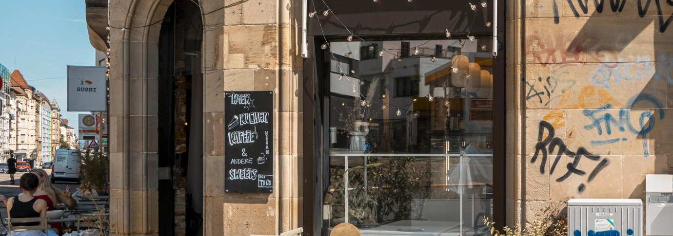 Caf&eacute; mit Au&szlig;enbestuhlung, Graffiti an der Wand, Lichterketten &uuml;ber dem Eingang. Schild mit "Kaffee & Kuchen". Stadtstra&szlig;e im Hintergrund., &copy; SMG, Sarah Schmid