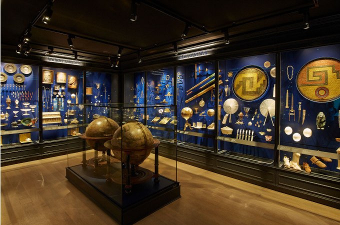 Museum exhibition with antique objects in display cases, including two large globes. The walls are illuminated in blue., &copy; Landesmuseum W&uuml;rttemberg