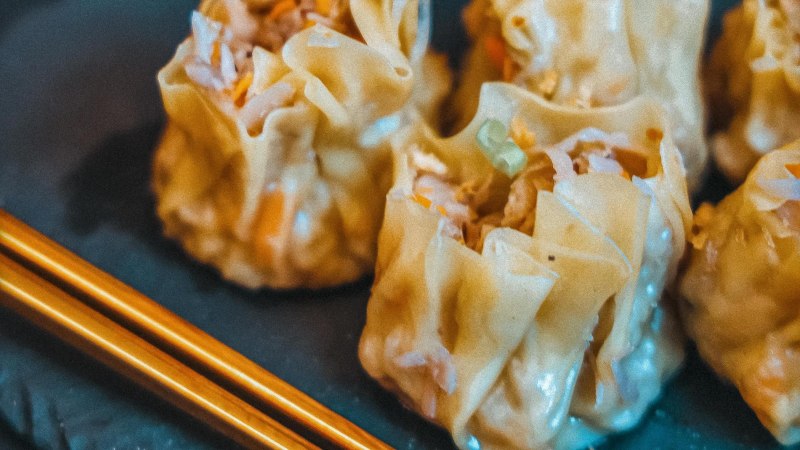 Nahaufnahme von gedämpften Dumplings mit Stäbchen auf einem Teller. Die Dumplings sind gefüllt und haben eine helle, glänzende Oberfläche., © Cäff Chen, Stuttgart