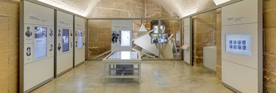 Interior view of the Stauffenberg memorial with modern exhibition walls, interactive displays and a central table in a vaulted room., © Daniel Stauch Photography