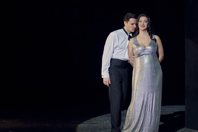 Ein Mann im Smoking und eine Frau im silbernen Abendkleid stehen eng beieinander auf einer B&uuml;hne, in dramatischer Beleuchtung., &copy; W&uuml;rttembergische Staatstheater Stuttgart
