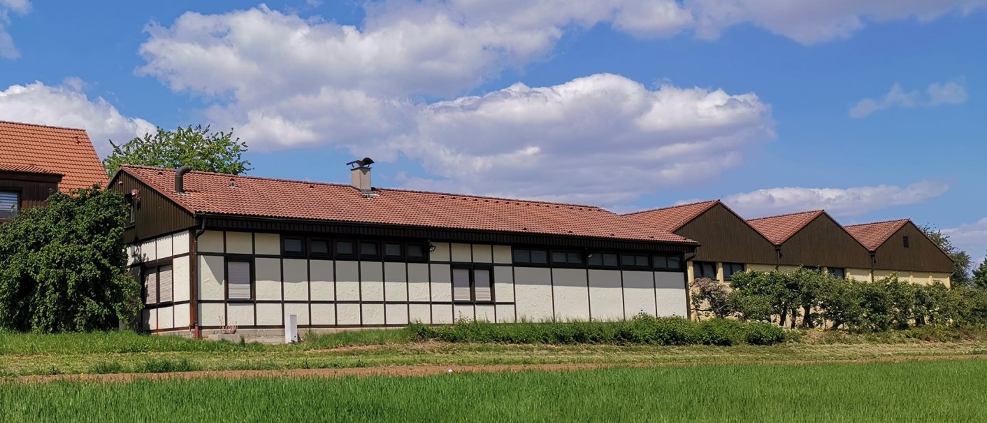 Half-timbered building with a red tiled roof, surrounded by green vegetation, under a blue sky with white clouds., © Weinbau Glock und Sohn GbR