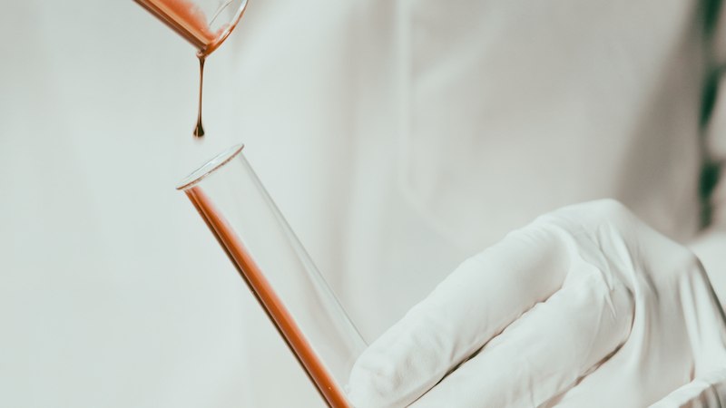 Eine Flüssigkeit tropft aus einem Reagenzglas in ein anderes. Eine behandschuhte Hand hält das untere Glas., © Theater Rampe Eine Flüssigkeit tropft aus einem Reagenzglas in ein anderes. Eine behandschuhte Hand hält das untere Glas., © Theater Rampe