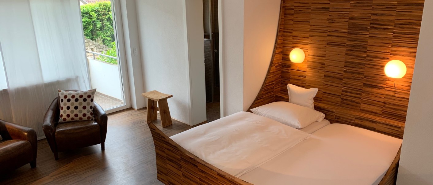 Modernes Schlafzimmer mit Holzdekor, Doppelbett, zwei Sesseln und Zugang zu einem kleinen Balkon., © TOMAS Modernes Schlafzimmer mit Holzdekor, Doppelbett, zwei Sesseln und Zugang zu einem kleinen Balkon., © TOMAS